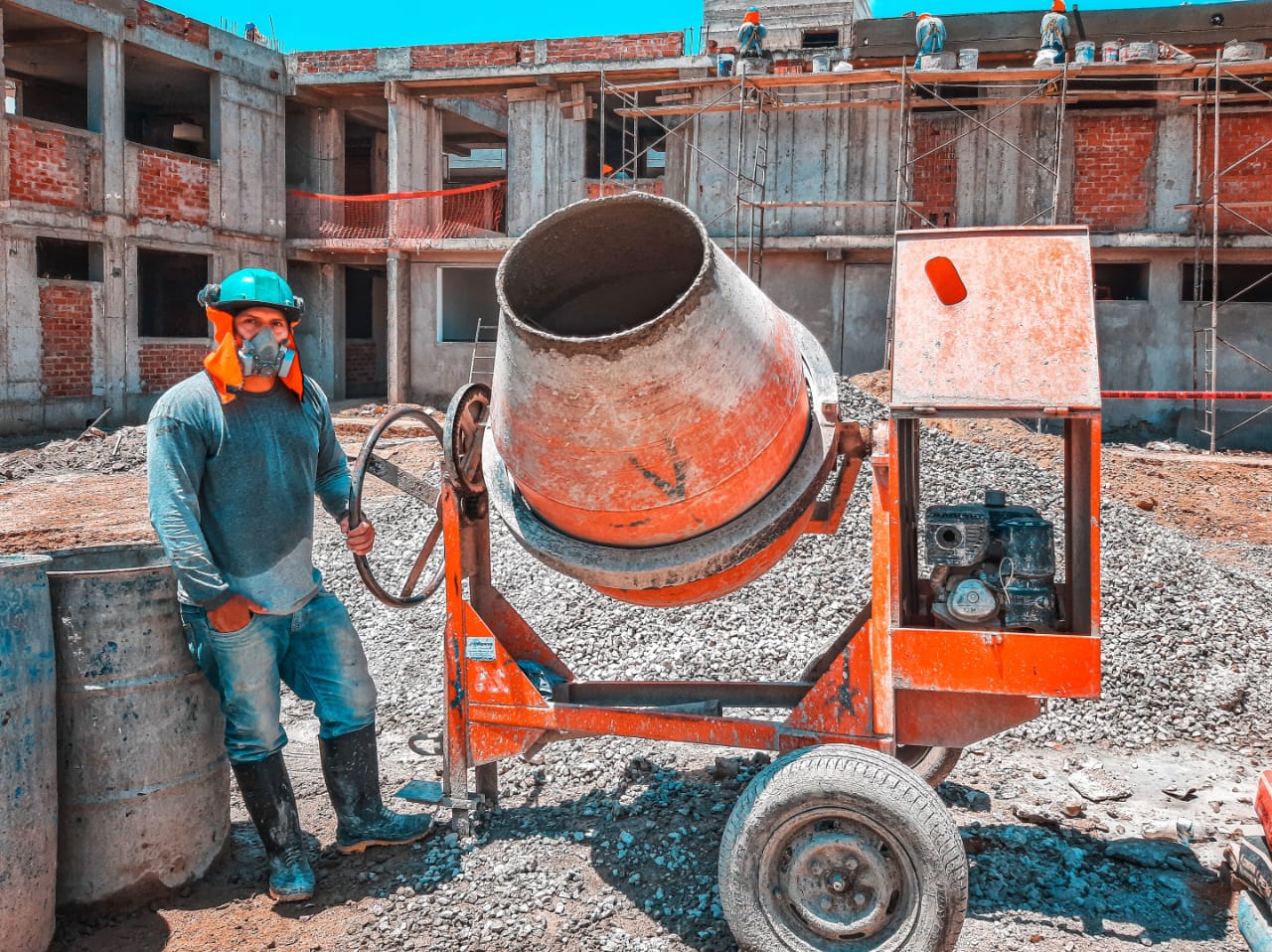Site worker in protective gear standing beside a concrete mixer at a multi-storey site